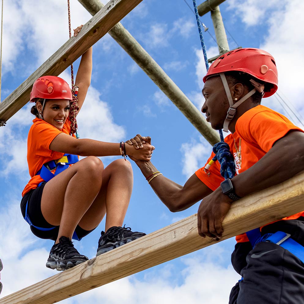 two campers on the ropes course wearing orange Camp Harbor View t-shirts 