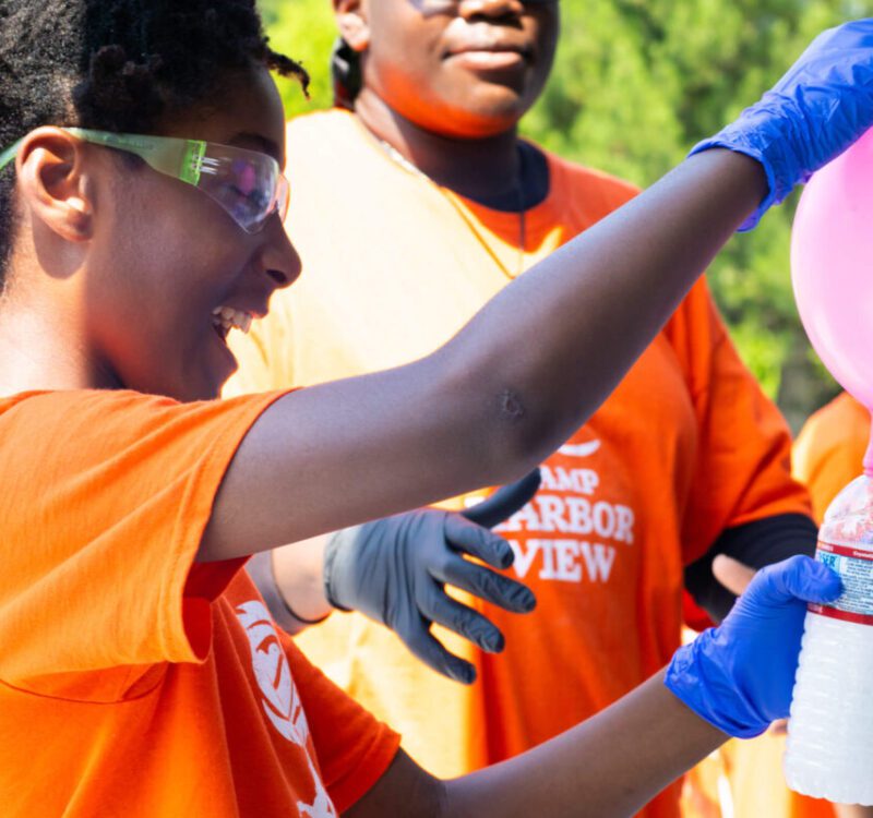 A camper smiles as they perform a science experiment with a balloon