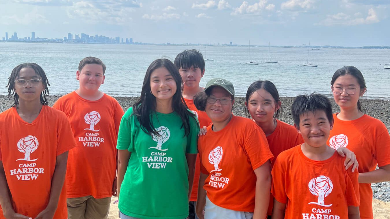 group of teens standing on the beach smiling with Boston skyline in the background