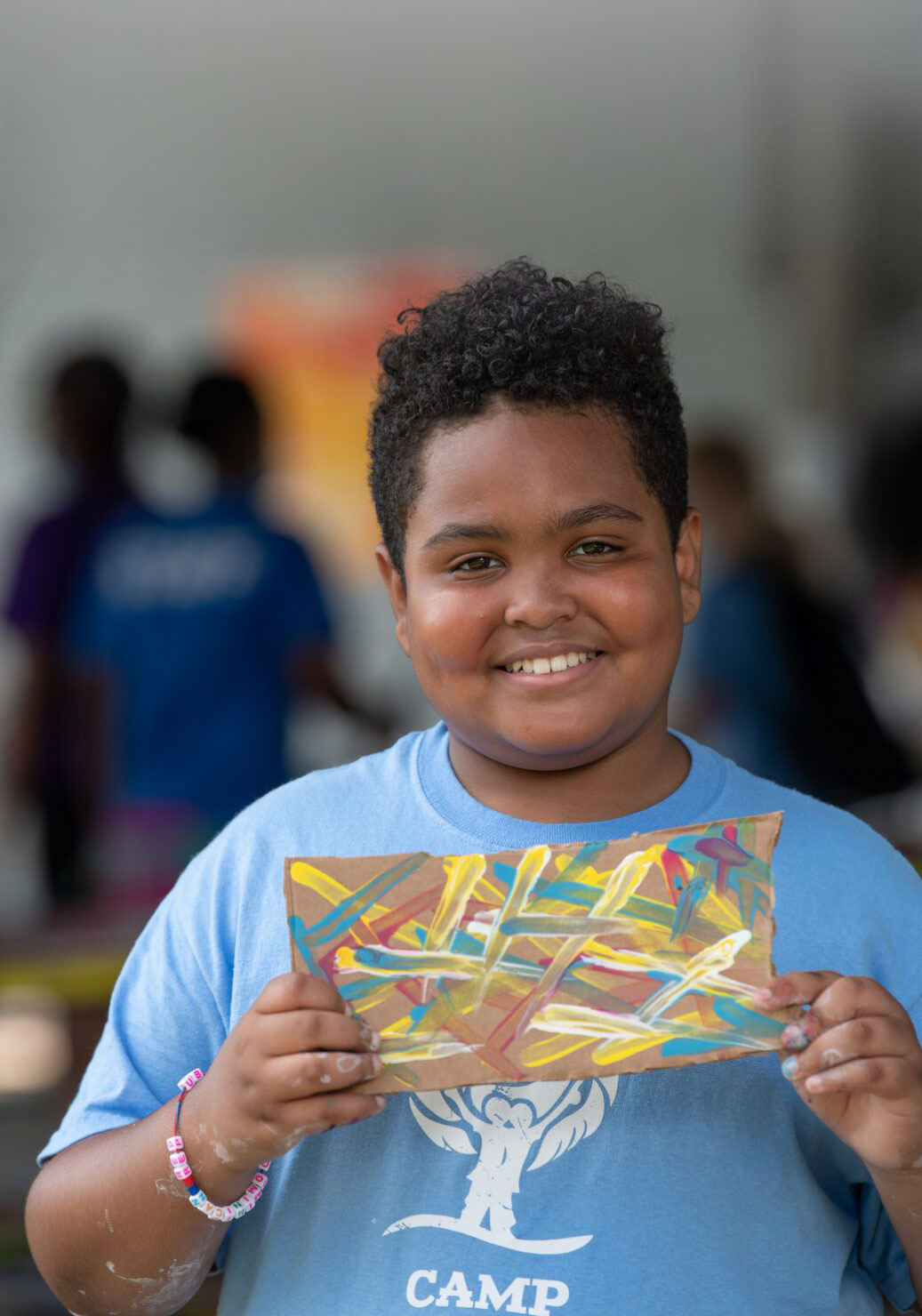 Camper in blue shirt smiling and holding up artwork