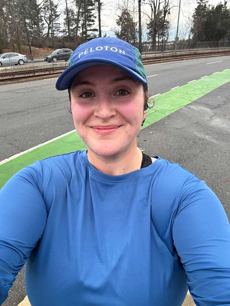 Woman taking a post-run selfie on a city street, wearing a blue athletic top and cap.