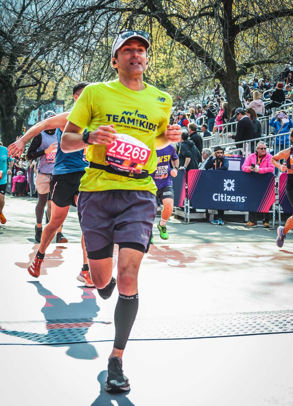 Man running in a marathon wearing a bright yellow shirt and race bib, with spectators lining the course.