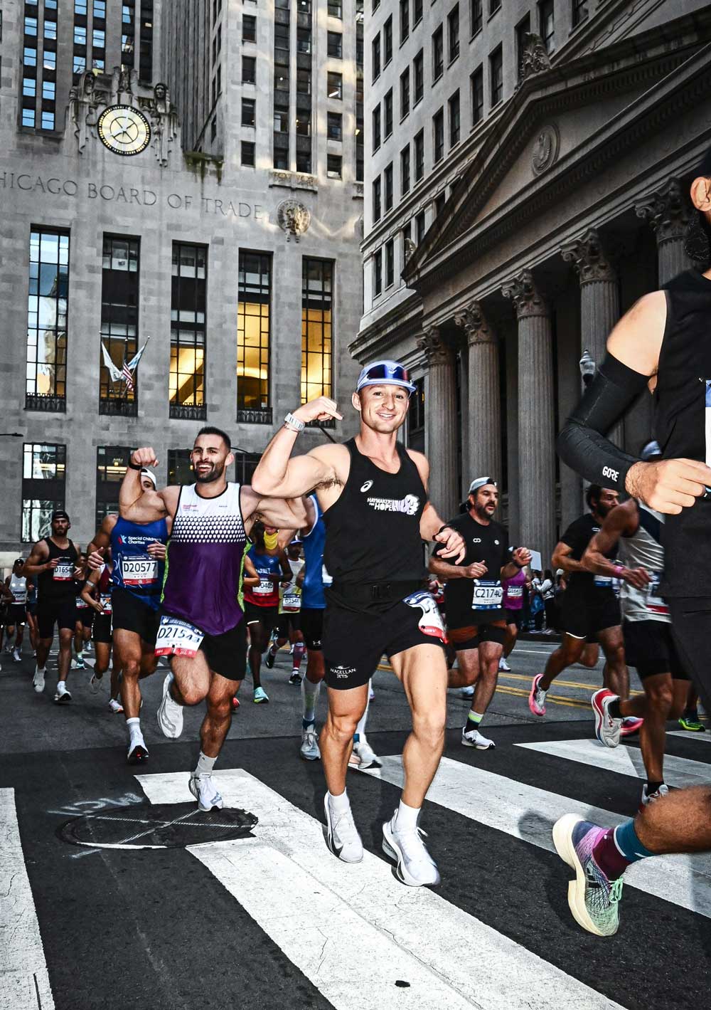 Young man running in a road race wearing a black shirt and race bib, mid-stride on a city street.