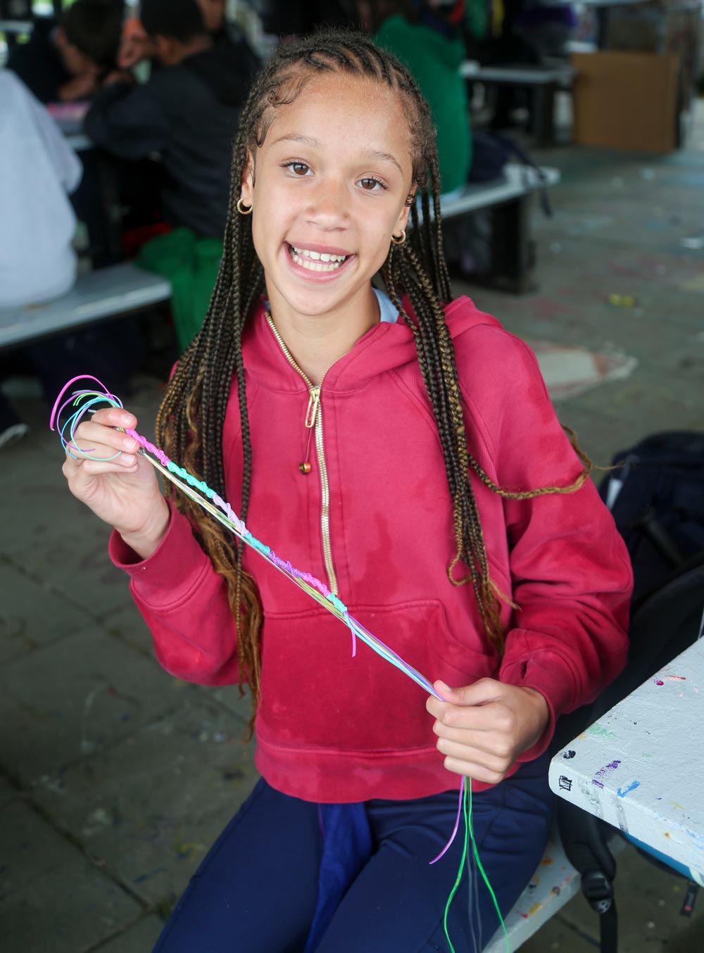 girl with long braids and pink sweatshirt making a bracelet at arts and crafts at camp