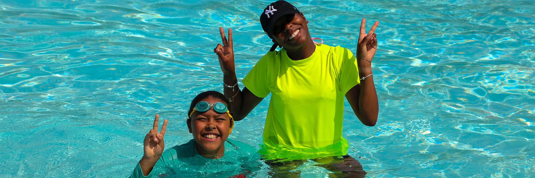 A camper and a counselor smile in a pool.