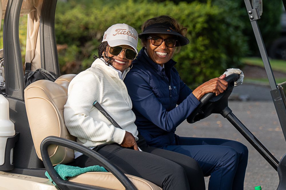 two women ride a golf cart at the CHV Golf Classic.